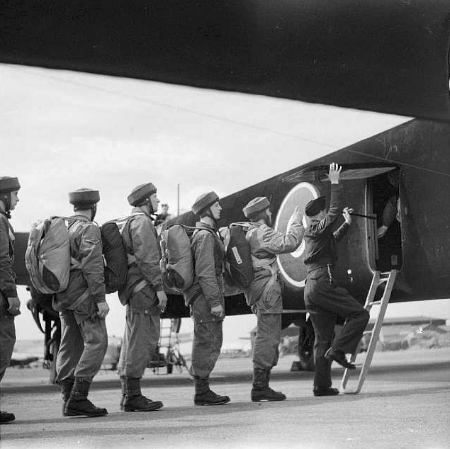 Troops at RAF Ringway, lined up at the rear door of an aircraft, waiting to climb onboard.